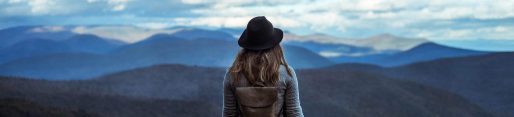 woman with hat on standing on mountain from behind