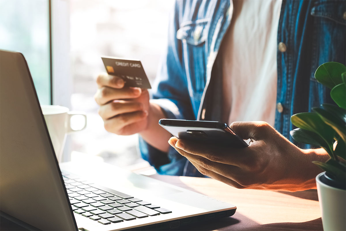 person holding a phone and credit card in front of laptop