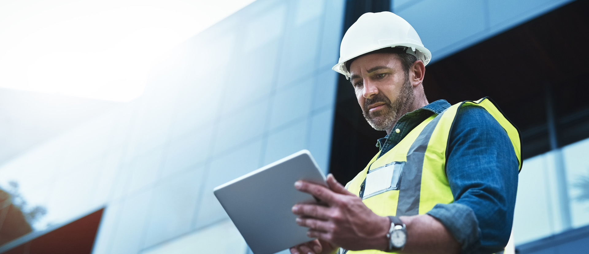 person wearing safety vest and hardhat holding a smart tablet