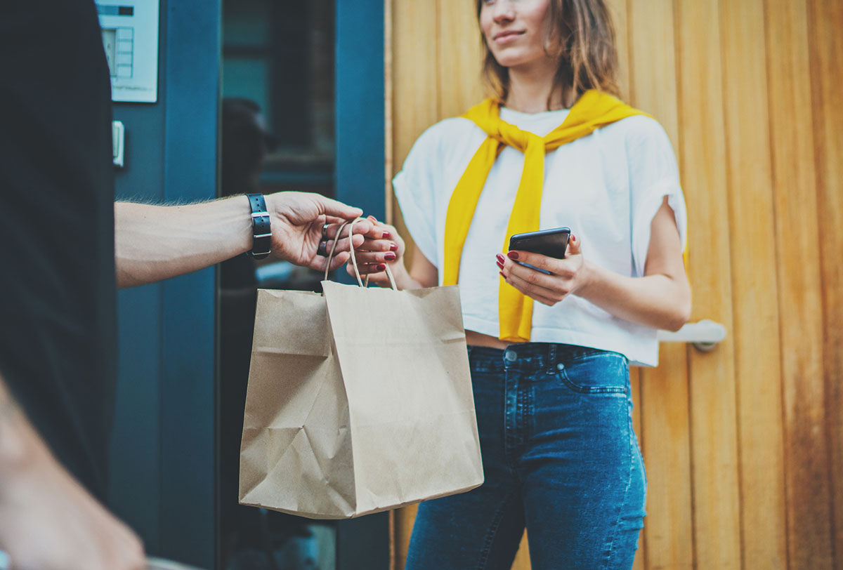 person handing bag of groceries to a customer at their home